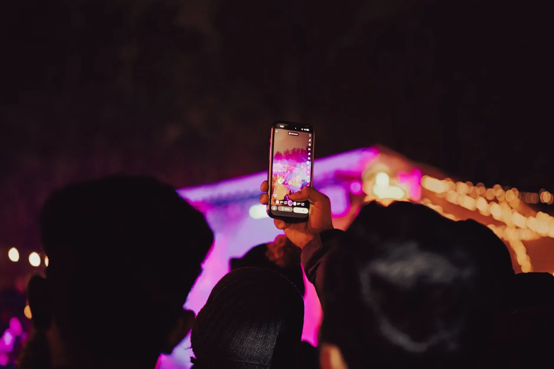 Publikum fotograferer en koncert i gang med smartphones under kraftige scenelys. Billedet indfanger den energiske stemning fra en live-aften.