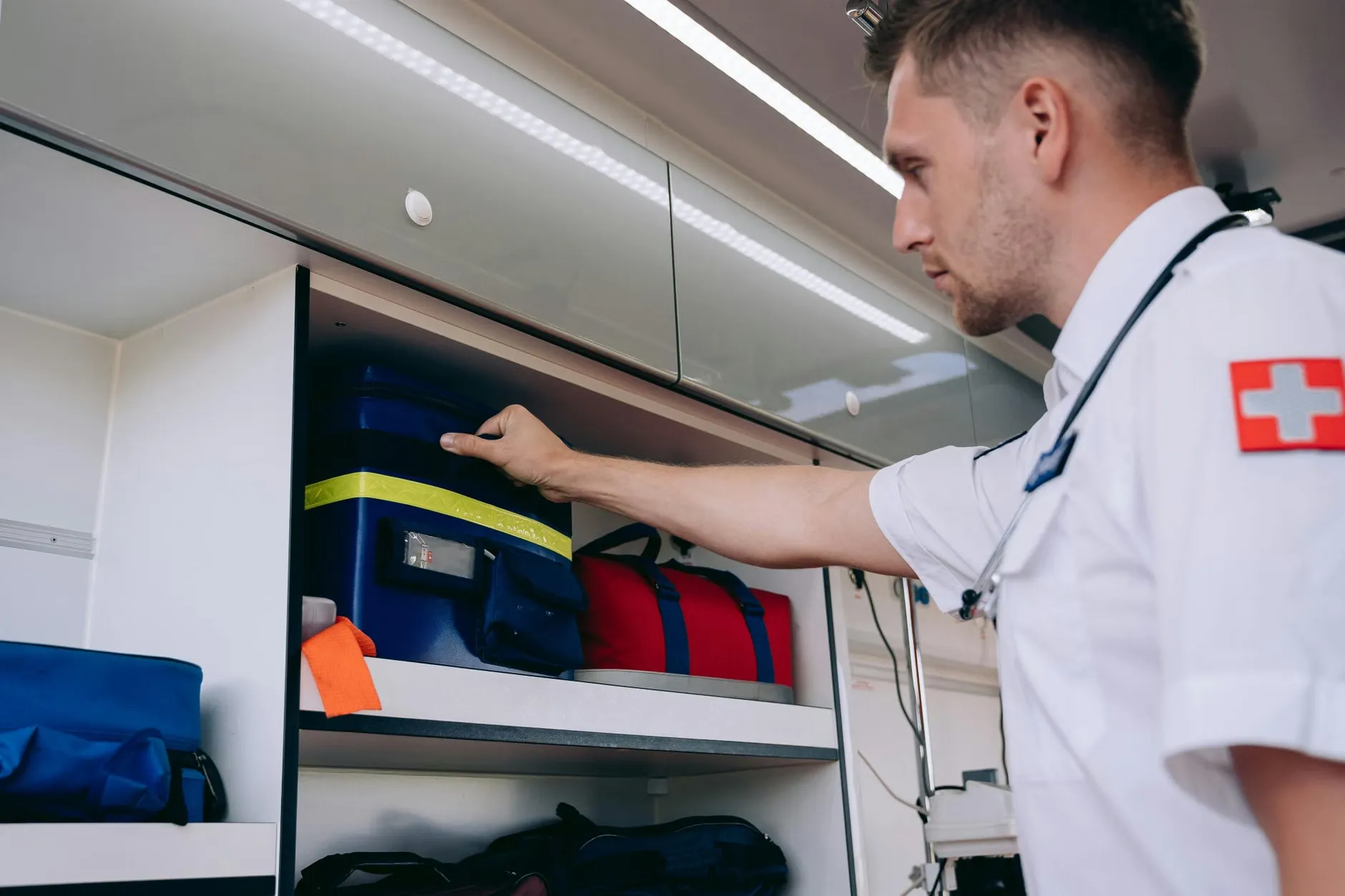 En paramediciner arrangerer medicinske forsyninger i en hylde i en ambulance som led i beredskab. Billedet illustrerer forberedelse til nødsituationer.