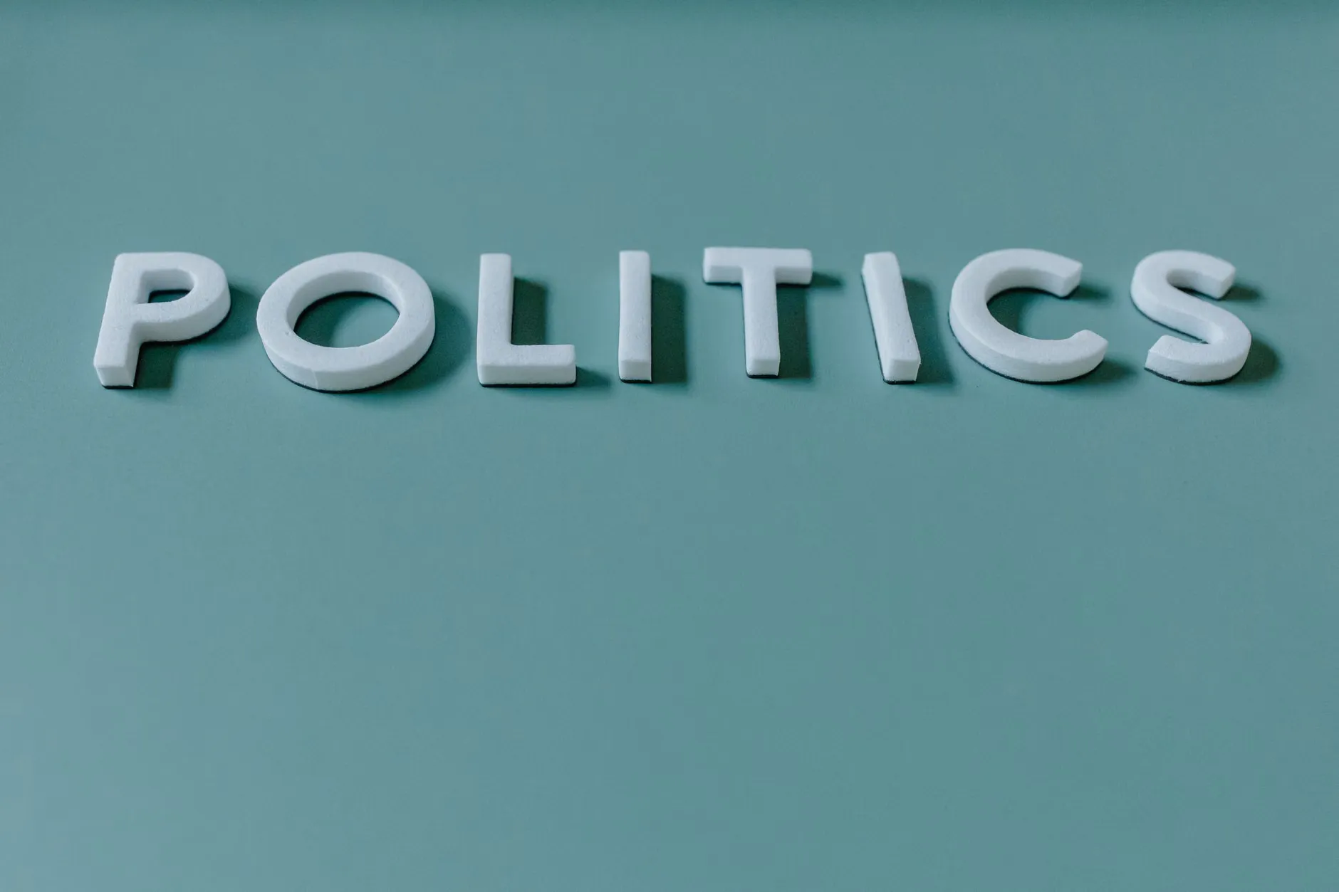 Tæt op på ordet 'Politik' mod en tealgrøn baggrund, der fremhæver politiske temaer.