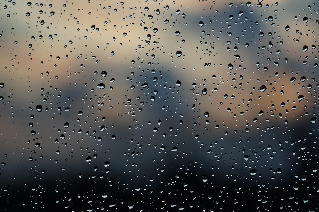 Et billede af regn, der falder mod en vinduesrude, symboliserende en regnfuld aften. Billedet viser også en mørk og stormfuld himmel.