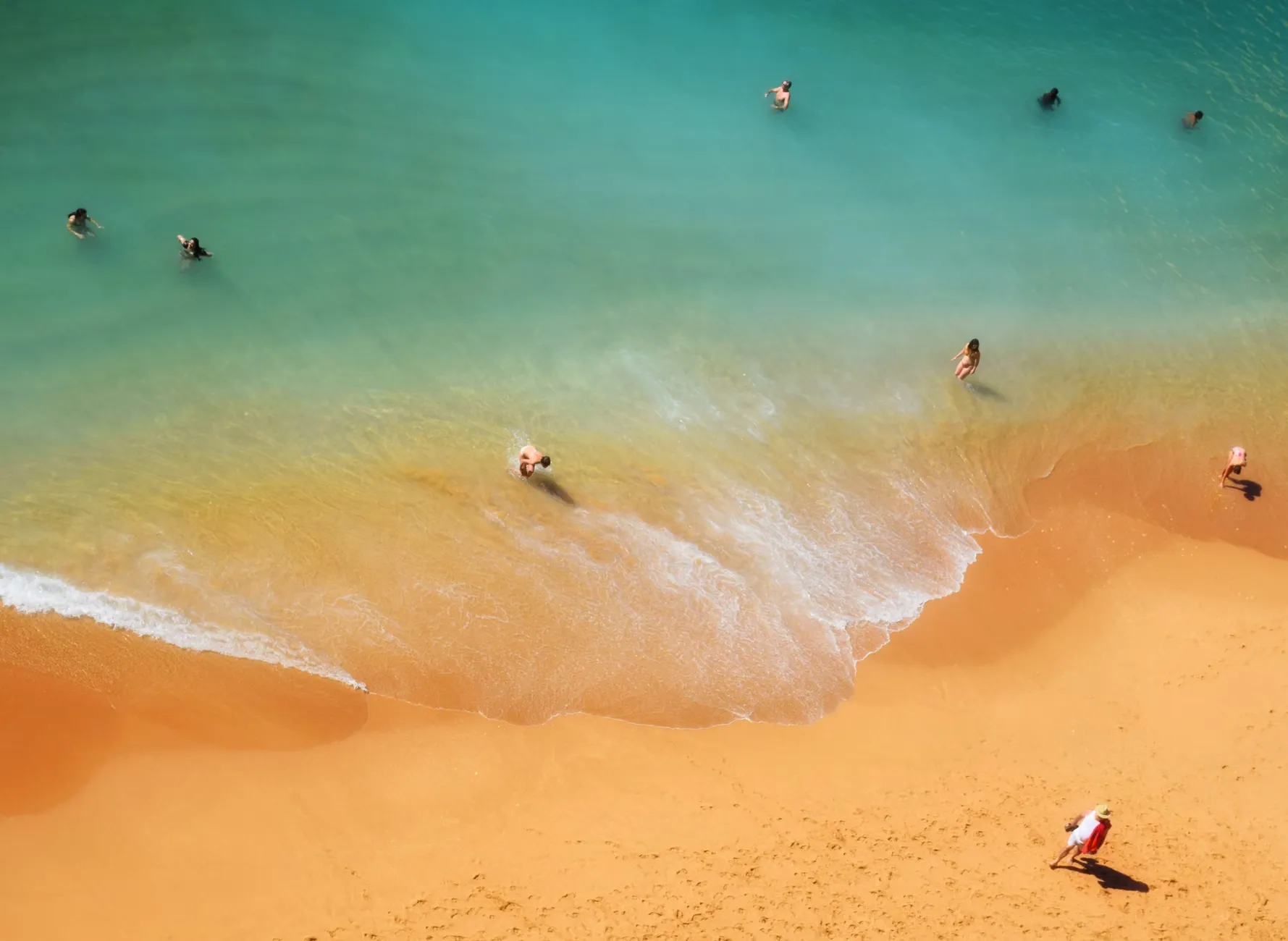 En scenic aerial visning af mennesker, der svømmer og slapper af på en sandstrand under solen.