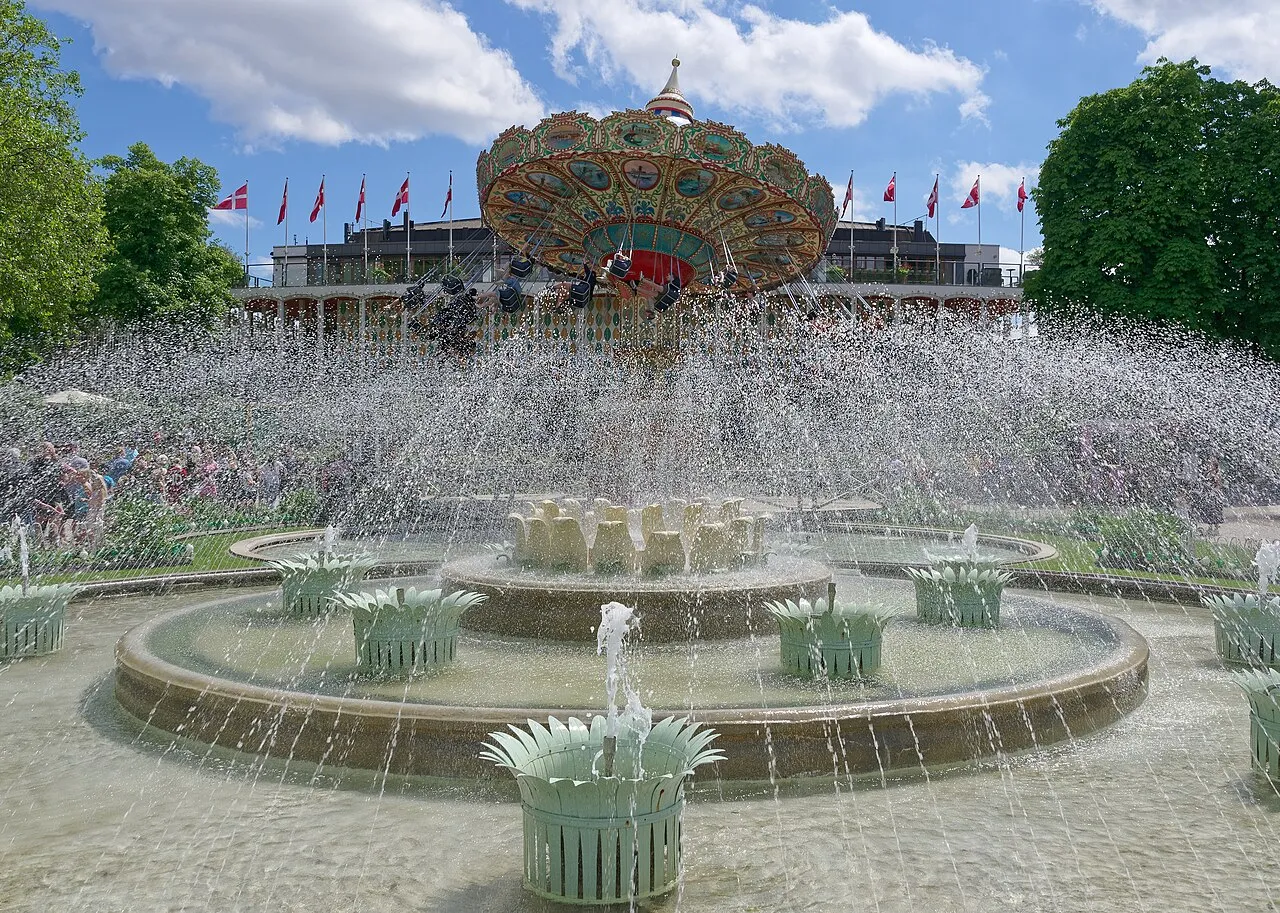 Et stemningsfuldt springvand i Tivoli Gardens med parkens grønne omgivelser i baggrunden. Billedet fanger vandets bevægelse og refleksioner i haven.